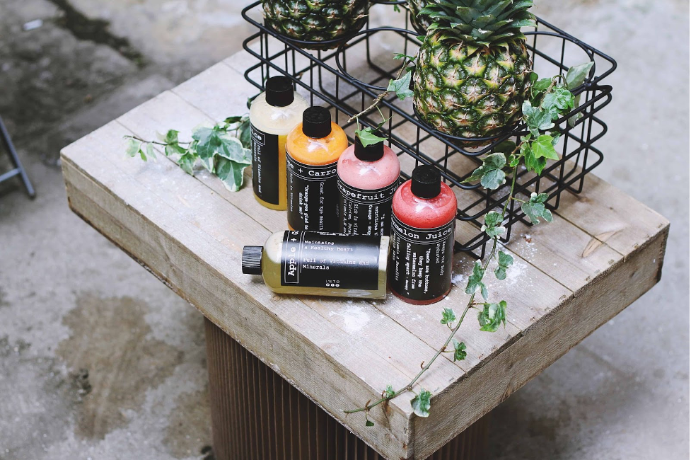 Cuatro recipientes de jugos, con una cantas al lado que contiene una piña. Todo sobre una tabla de madera